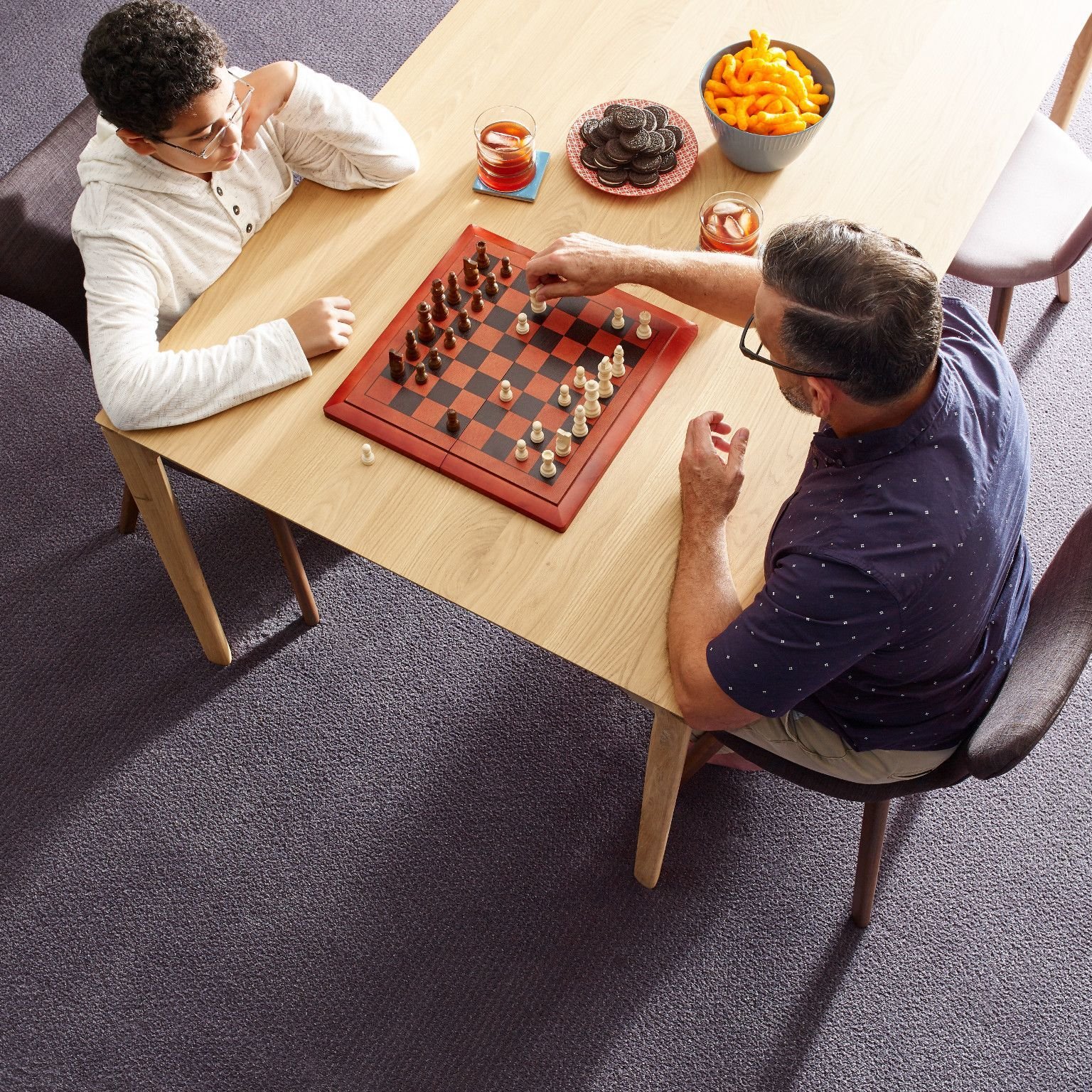 two men playing chess at a wooden table in a room with purple carpet from Northcraft Flooring & Design in Raytown, MO